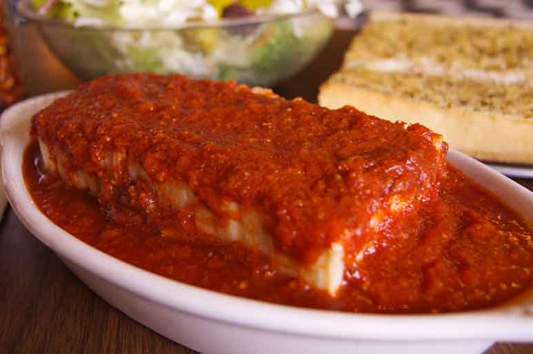 lasagna drizziled with Roma's famous meat sauce, garlic bread, and salad on a dinner table