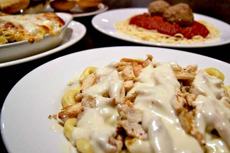 chicken alfredo on one plate and sphagetti on another with a baked lasagna caserol